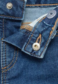 Blugii din denim au o nuanță închisă de albastru, cu cusături aurii contrastante, un nasture argintiu și o căptușeală interioară de un albastru deschis.