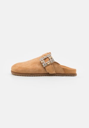 Lysebrun ruskind slip-on sko med stor dekorativ rhinsten spænde på siden og flad gummisål.