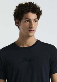 Donkerblauwe katoenen T-shirt met een textuur van het "Original Penguin" logo op de borst. Klassiek ontwerp met ronde hals en korte mouwen.