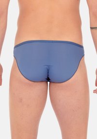Blaue Badehose aus glattem, elastischem Stoff. Verfügt über einen niedrigen Bund und ein abgerundetes Rückendesign mit minimalen Nahtdetails.