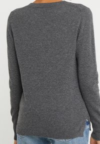 Suéter de punto gris con mangas largas, escote redondeado y dobladillos acanalados. Textura suave, forma ajustada y detalles de abertura lateral.