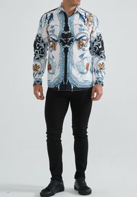 Chemise à manches longues avec une base blanche ornée de motifs bleus, noirs et floraux. Fabriquée en tissu avec des manches et un col noirs contrastants.