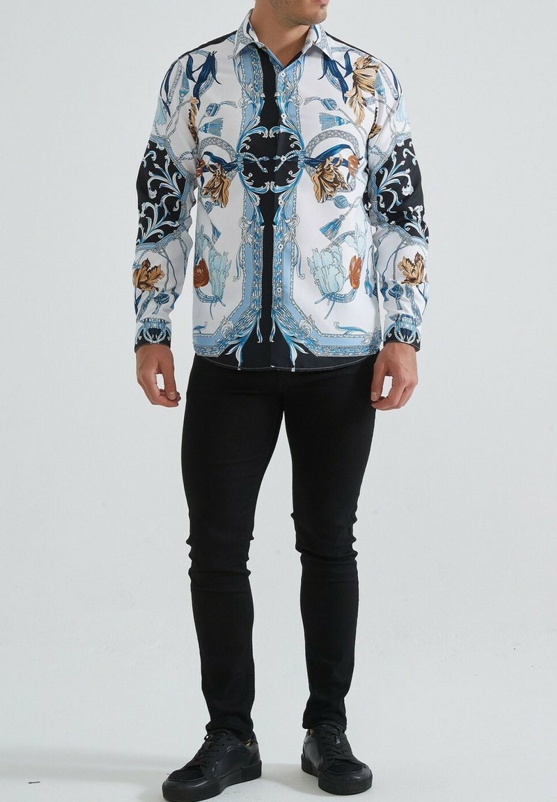 Chemise à manches longues avec une base blanche ornée de motifs bleus, noirs et floraux. Fabriquée en tissu avec des manches et un col noirs contrastants.