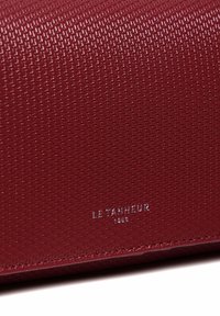 Portefeuille en cuir texturé rouge avec une finition lisse, le nom de la marque en relief et un subtil détail de couture le long du bord.