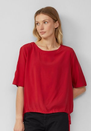 Blouse rouge à manches courtes en tissu léger avec un col rond et un ourlet élastique froncé. Texture lisse avec une coupe décontractée.