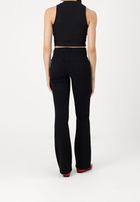 Jean flared negros con cintura alta, de tela de algodón, y dos bolsillos traseros; combinado con un top corto negro y zapatos rojos.