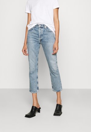 Jeans en denim bleu clair, coupés, avec taille haute, coupe droite et ourlet effiloché. Associés à un t-shirt blanc et des mules noires.
