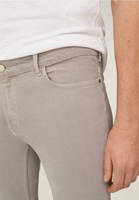 Jeans de denim gris con corte ajustado, que cuentan con un bolsillo delantero, herrajes metálicos y detalles de costura sutiles. Textura suave y acabado liso.