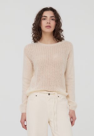 Maglione lavorato a maglia color beige chiaro con trama ariosa, collo rotondo e maniche lunghe, abbinato a pantaloni bianchi a vita alta. Tessuto morbido.