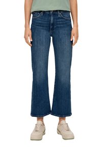 Blå denimjeans med rak bendesign, midjehöjd och uppvikt fåll. Bärs med en ljusgrön skjorta och beiga sneakers.