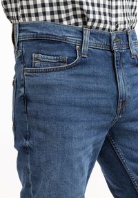 Granatowe dżinsy z pięcioma kieszeniami, z widocznymi szwami i delikatnym wyblaknięciem. W połączeniu z czarno-białą koszulą w kratę.