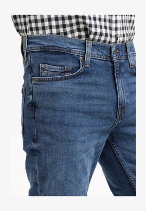 Granatowe dżinsy z pięcioma kieszeniami, z widocznymi szwami i delikatnym wyblaknięciem. W połączeniu z czarno-białą koszulą w kratę.