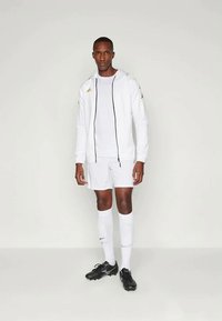 Valge sportlik riietus, mis sisaldab tõmblukuga jakki, särki, lühikesi pükse ja pikka sokki. Mustad spordijalatsid. Kuldsed aktsendid jakil.