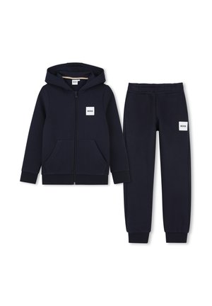 Marineblauwe zip-up hoodie en bijpassende joggingbroek met BOSS-logo patches op borst en dij, plat neergelegd op een witte achtergrond.