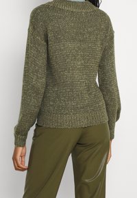 Maglione lavorato a maglia in verde oliva, con un motivo testurizzato, orlo a coste e maniche lunghe, abbinato a pantaloni verdi oliva.