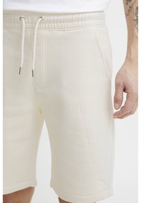 Lys beige bomullsblandingsshorts med elastisk midje, snøring, sidelommer og en subtil logo brodert nær kanten.