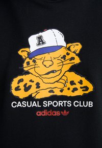 Sort stof med en gul tegneserieleopard med sorte pletter, iført en hvid og blå kasket. Teksten lyder "CASUAL SPORTS CLUB" og "adidas."