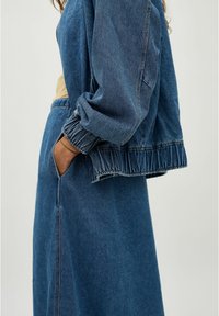 Chaqueta de mezclilla con mangas anchas y fruncidas y un dobladillo deshilachado. Cuenta con un cierre de cremallera y bolsillo lateral, en un lavado azul medio.