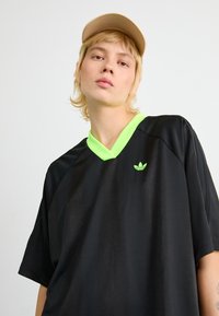 Svart sportt-shirt med kort ärm och v-ringning, prydd med en neongrön krage och en liten grön logotyp. Slät textur och lätt material.