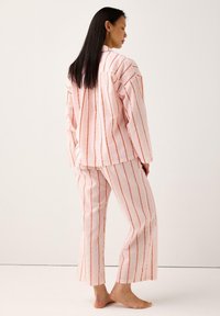 Rosa randig pyjamaset som består av en långärmad topp och matchande byxor med avslappnad passform, tillverkat av texturerad tyg med horisontella ränder.