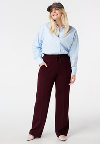 Lichtblauw overhemdd met speelse patronen, gecombineerd met bordeauxrode broeken met elastische tailleband en een gestreepte pet. Beige schoenen maken de look af.