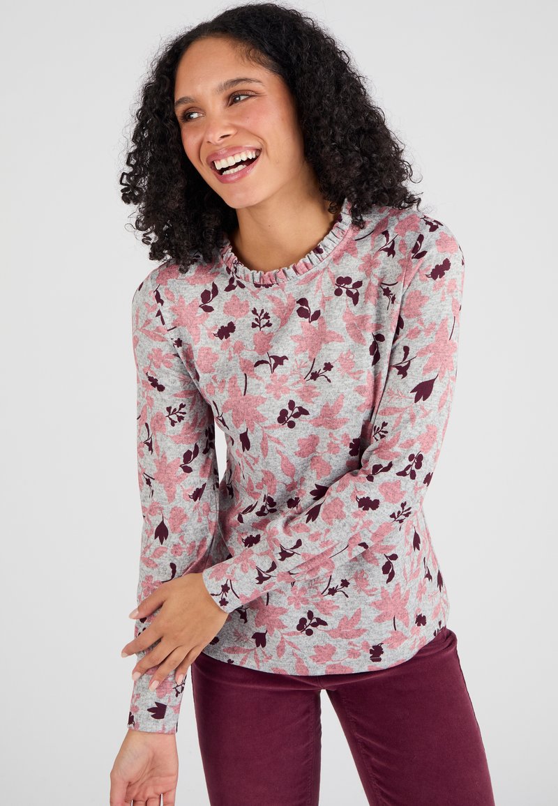 Lange mouwen top in lichtgrijs met een roze en bordeauxrode bloempatronen, met een gerimpelde halslijn en een getailleerd ontwerp. Gecombineerd met bordeauxrode broek.