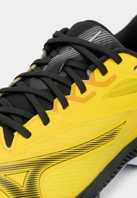 Chaussure de sport jaune avec des accents noirs, surface texturée et lacets noirs. Possède un motif rayé près de l'orteil et un col rembourré.