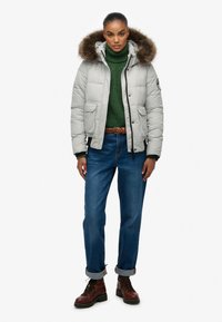 Grå polstret jakke med pelsforet hætte, grøn striktrøje, blå jeans og brune snørebåndsstøvler. Har sidelommer og elastiske manchetter.