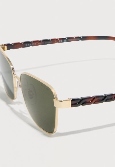 Γυαλιά ηλίου με χρυσή κορνίζα, σκούρους πράσινους φακούς και βραχίονες με σχέδιο χελώνας, σε λευκό φόντο.