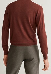 Maglione color marsala con maniche lunghe, polsini e scollatura a coste, abbinato a pantaloni grigi a fantasia con una vestibilità slim.