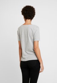 Maglietta in cotone grigia con scollo rotondo e maniche corte, caratterizzata da una texture liscia e un design aderente, abbinata a jeans neri.