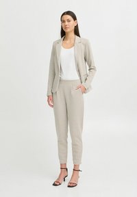 Lysegrå skreddersydd blazer og matchende tettsittende bukser, kombinert med en hvit topp. Stoffet har en subtil tekstur, og buksene har sidelommer.