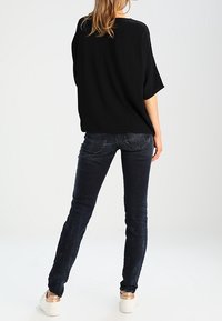 Sort oversized top med korte ærmer, parret med mørkeblå slim fit jeans. Outfitet har et minimalistisk design og casual fodtøj.