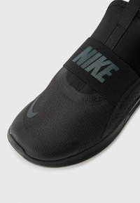 Black athletic shoe with a mesh upper, elastic strap, and rubber sole. Features a shiny black Nike logo and sleek design.