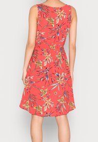 Robe florale rouge sans manches, avec une taille cintrée et une jupe évasée. Le tissu a une texture lisse et des motifs floraux colorés.