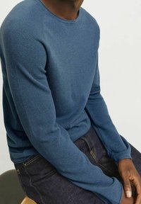 Blå stickad crew neck-tröja med långa ärmar, med en texturerad tyg och en avslappnad passform, i kombination med mörk denimjeans.