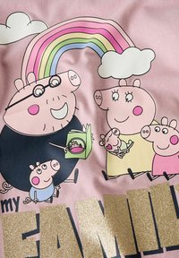 Różowy materiał z kreskówkowymi świniami, tęczą nad głową i błyszczącym złotym tekstem "moja RODZINA". Zauważalne szczegóły to okulary i zielona książka.