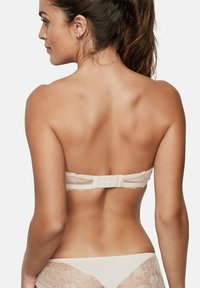 Soutien-gorge bandeau en dentelle beige avec un bord festonné délicat et une fermeture à crochets et œil au dos. Matière lisse et satinée sur l'ensemble.