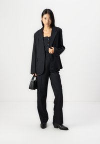 Svart pinstripesett med en strukturet blazer og tilpassede bukser, kombinert med en svart skjorte og svart håndveske.