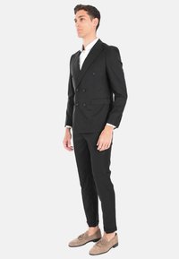 Giacca nera doppiopetto con sei bottoni, abbinata a pantaloni slim fit e scarpe in suede chiare. Camicia bianca fresca sotto.