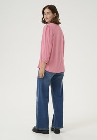 Blouse rose texturée avec des manches trois quarts, associée à un jean large bleu et des chaussures compensées noires. Design clair et simple.