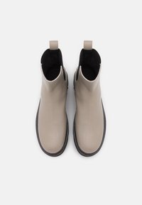 Botas de tobillo de cuero beige con acabado liso, paneles laterales elásticos y suela de goma negra. Incluye una pequeña lengüeta en la parte trasera.