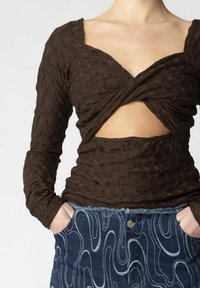 Brun, tekstureret bluse med lange ærmer og indpakningsdesign samt udskæring i taljen, parret med en blå denim-nederdel med bølge-lignende mønstre.