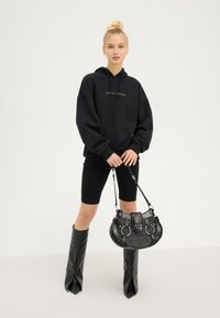 Hanorac supradimensionat negru cu logo, pantaloni scurți negri pentru bicicletă, botine cu vârf ascuțit până la genunchi și o geantă texturată neagră cu accente de hardware și bretele.