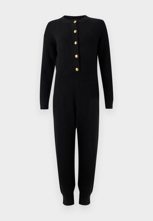 Tuta nera in maglia a coste con maniche lunghe, bottoni dorati sul davanti, vita aderente e gambe affusolate che terminano con polsini.