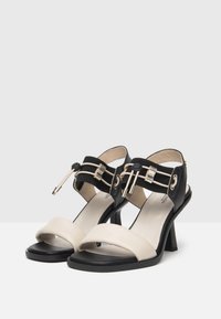 Black and beige high-heeled sandals with a textured upper, wide front straps, and decorative hardware accents on the ankle strap.