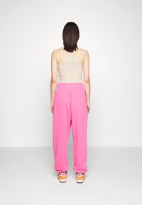 Rosa joggingbyxor med elastisk midja, kombinerat med en beige linne och flerfärgade sneakers, sedd bakifrån mot en enfärgad bakgrund.