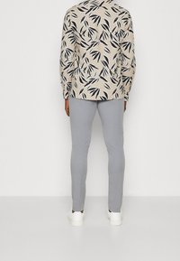 Camisa con estampado floral en beige con hojas negras, combinada con pantalones ajustados gris claro y zapatillas blancas. Tela transparente y corte entallado.