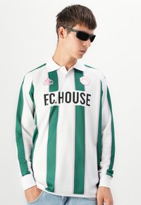 Pitkät hihat omaava polo-paita, jossa on vihreitä ja valkoisia pystysuoria raitoja, joissa on vaaleanpunaisia yksityiskohtia. Rintaan on painettu suurilla mustilla kirjaimilla "F.C.HOUSE" ja Kappa-logo.