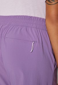 Light purple athletic shorts with an elastic waistband and drawstring; side pocket with a stitched opening for secure storage.